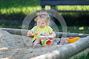 Happy toddler girl playing in sand on outdoor playground. Baby having fun on sunny warm summer sunny day. Active child