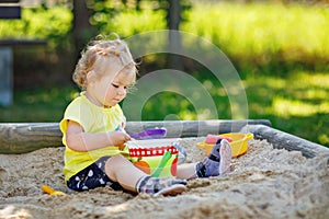 Happy toddler girl playing in sand on outdoor playground. Baby having fun on sunny warm summer sunny day. Active child