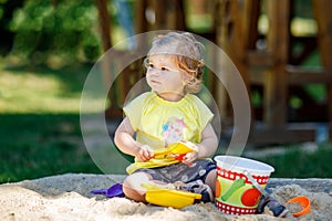 Happy toddler girl playing in sand on outdoor playground. Baby having fun on sunny warm summer sunny day. Active child