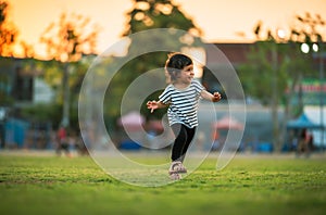 happy toddler girl running on grass field in park at sunset