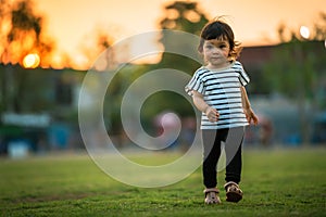happy toddler girl walking on grass field in park at sunset
