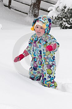 Happy toddler girl in warm coat and knitted hat tossing up snow and having a fun in the winter outside, outdoor portrait