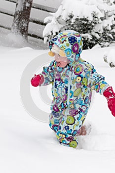 Happy toddler girl in warm coat and knitted hat tossing up snow and having a fun in the winter outside, outdoor portrait