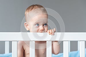 Happy toddler playing in crib, with a cute smile, exploring their world with nose, cheek, eye, eyelash, and thumb