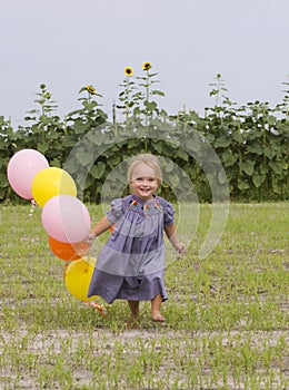 Happy toddler running with balloons in field