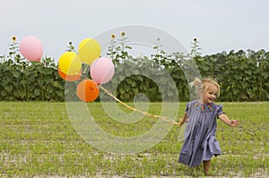 Happy toddler running with balloons in field