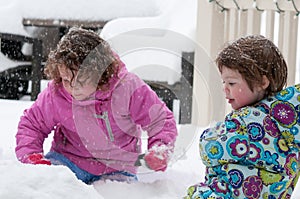 Happy toddler sibling girls in warm coat and knitted hat tossing up snow and having a fun in the winter outside, outdoor