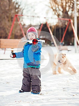 Happy toddler white Caucasian boy running and playing with snow and white large big pet dog