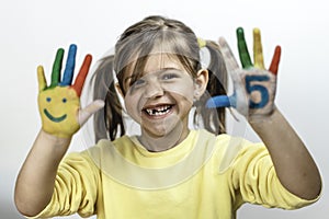 Happy toothless little girl with the five number painted on the hand laughing and having fun - Little girl painting her hands with