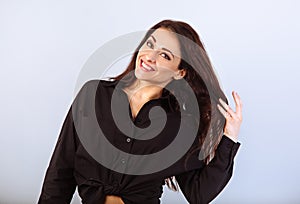 Happy toothy laughing woman posing in black shirt standing and holding hand the healthy brown long hair on studio blue background