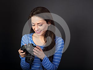 Happy toothy smiling young female photograph looking on the screen of camera and joying the photo on dark grey background