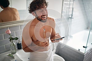 Happy topless man texting while brushing teeth