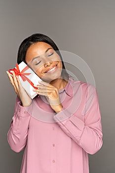 Happy touched young woman hold gift box at face with closed eyes pleasured with unexpected present