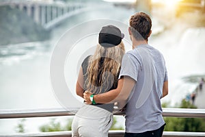 Happy tourist couple enjoying the view to Niagara Falls during romantic vacation. People looking to nature landscape at sunset tim