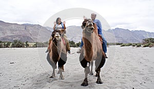 A happy tourist couple riding on double humped Bactrian camels