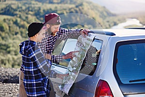 Happy tourist couple with paper map near car. Smiling young people using map. Traveling by rented car on summer