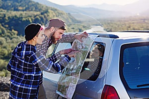 Happy tourist couple with paper map near car. Smiling young people using map. Traveling by rented car on summer