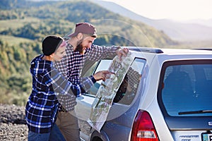 Happy tourist couple with paper map near car. Smiling young people using map. Traveling by rented car on summer