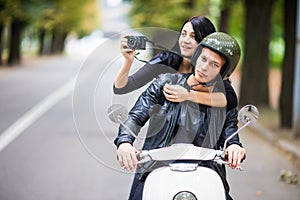 Happy tourist young couple on scooter ride in new city. Woman making photo on camera while riding outdoors