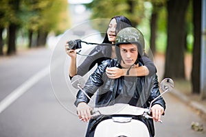 Happy tourist young couple on scooter ride in new city. Woman making photo on camera while riding outdoors