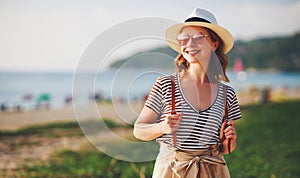 Happy tourist girl with backpack and hat on sea beach