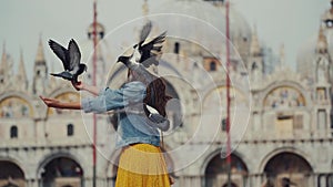 Happy tourist in hat play with pigeons, feeds them, having fun on San Marco