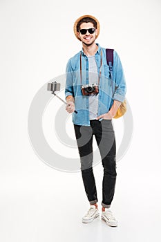 Happy tourist holding backpack, camera and smartphone on selfie stick