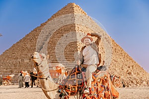 Happy Tourist man with hat riding on camel background pyramid of Egyptian Giza, sunset Cairo, Egypt