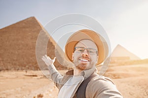 Happy tourist man in hat take selfie photo background pyramid of Egyptian Giza sunset, Cairo, Egypt