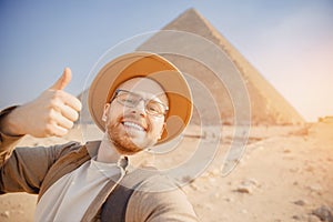 Happy tourist man in hat take selfie photo background pyramid of Egyptian Giza sunset, Cairo, Egypt