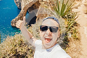 Happy tourist man taking selfie photo on background Blue Grotto in Malta