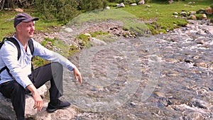 Happy tourist sitting on big stone on rapid river shore in mountain