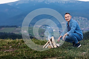 Happy tourist sitting by the fire, traveler smiling in the smoke of the fire. tourist smokes a fire on the mountain. selective