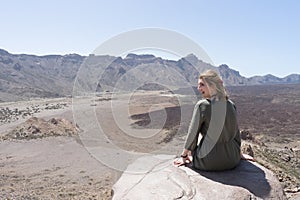 Happy tourist sitting in a rock of a viewpoint,with observation and relax in a volcanic desert