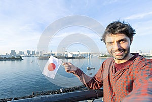 happy tourist taking selfie with smartphone and showing the japan\'s flag at bridge at tokyo in japan background.
