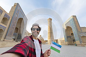 happy tourist traveling in Uzbekistan take selfie photo with uzbekistan flag in in front of the Kalyan minaret and mosque, Bukhara