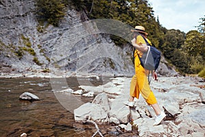 Happy tourist woman hiking by mountain river enjoying landscape. Traveler walking along rocks. Summer trip