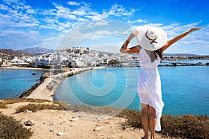 A happy tourist woman in a summer dress looks at the town of Naxos island