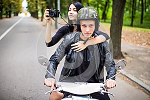 Happy tourist young couple on scooter. Woman making photo on camera while riding outdoors
