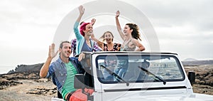 Happy tourists friends doing excursion in desert on convertible 4x4 car - Young people having fun traveling together - Friendship