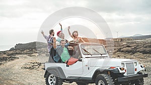 Happy tourists friends doing excursion on desert in convertible 4x4 car - Young people having fun traveling together - Friendship