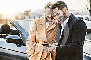 Happy tourists rents car on vacation - Adult couple checking insurance service on smart mobile phone device