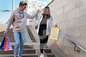 Happy tourists walk around city with purchases and souvenirs in their hands. Guy helps girl to go down the stairs