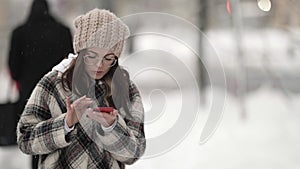 happy townswoman is walking alone in city at winter, using smartphone, sending messages in chat photo