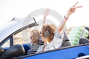 Happy travel adult friends lifestyle concept with couple of adult caucasian woman in a convertible car and luggage behind the