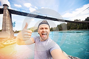 Happy travel blogger young man make selfie photo and taking on trip in Russia, background blue river Katun Altay