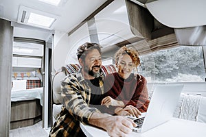 Happy travel couple lifestyle smile and use laptop together inside a modern camper van in vanlife offgrid alternative office