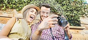 Happy travel couple watching photos on mirrorless camera - Young people having fun on summer vacation - Main focus on him -