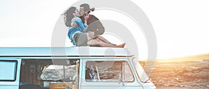 Happy travel influencers couple kissing on minivan roof at sunset with desert on background - Trendy people having fun traveling