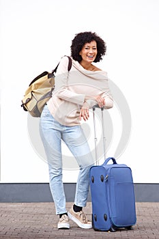 Happy travel woman standing with luggage by white wall